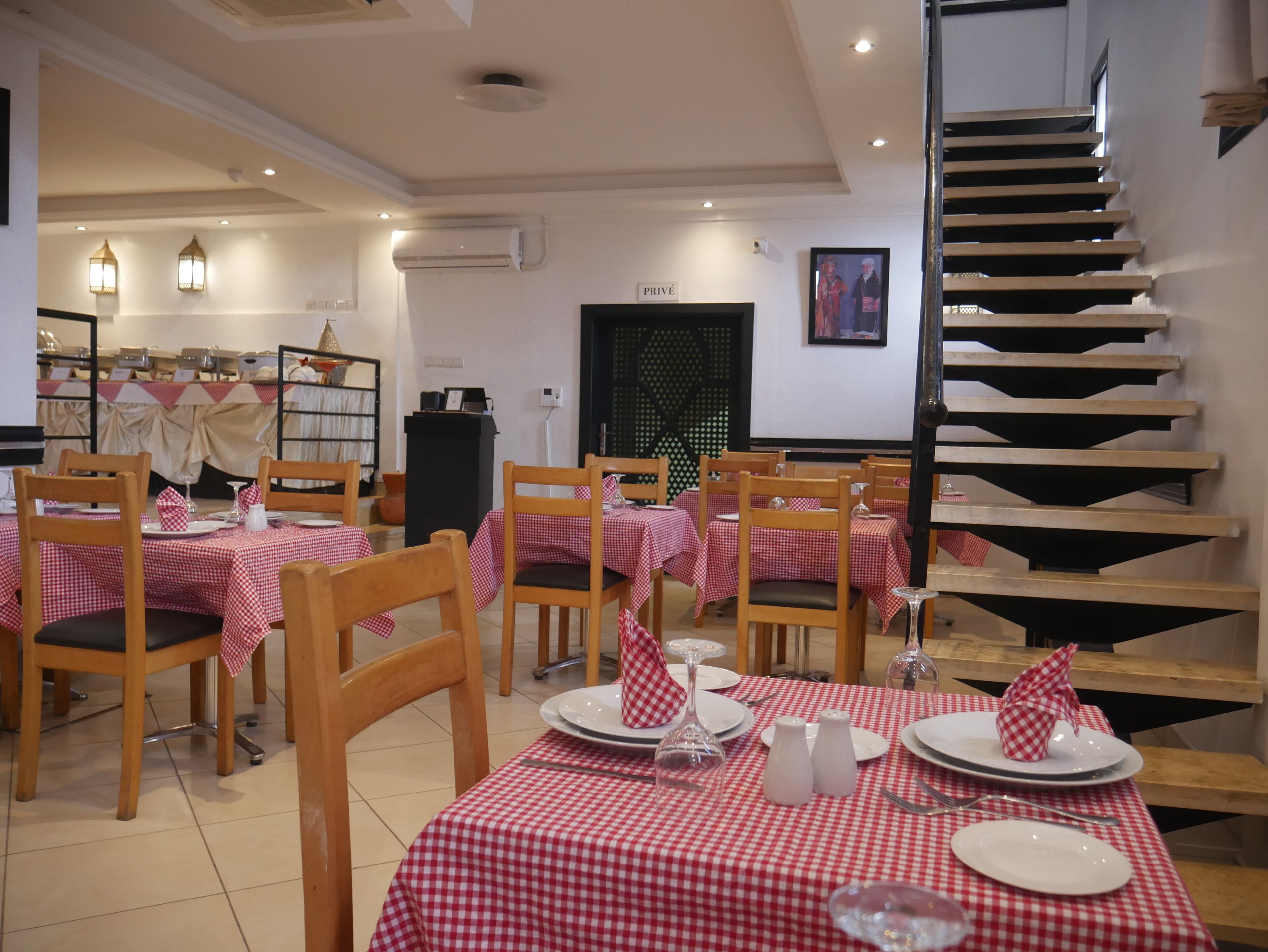 Un restaurante con manteles a cuadros, sillas de madera y una escalera.