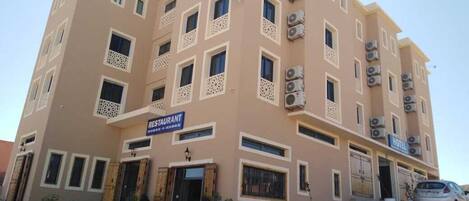 A multi-story hotel with a restaurant on the ground floor, air conditioning units, and outdoor seating.