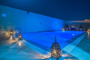 Una piscina con borde de baldosas, rodeada de faroles y una mesa con sillas.