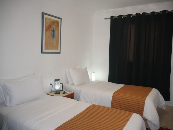 Habitación de hotel con dos camas, una mesita de noche con lámpara, un cuadro en la pared y una cortina negra.