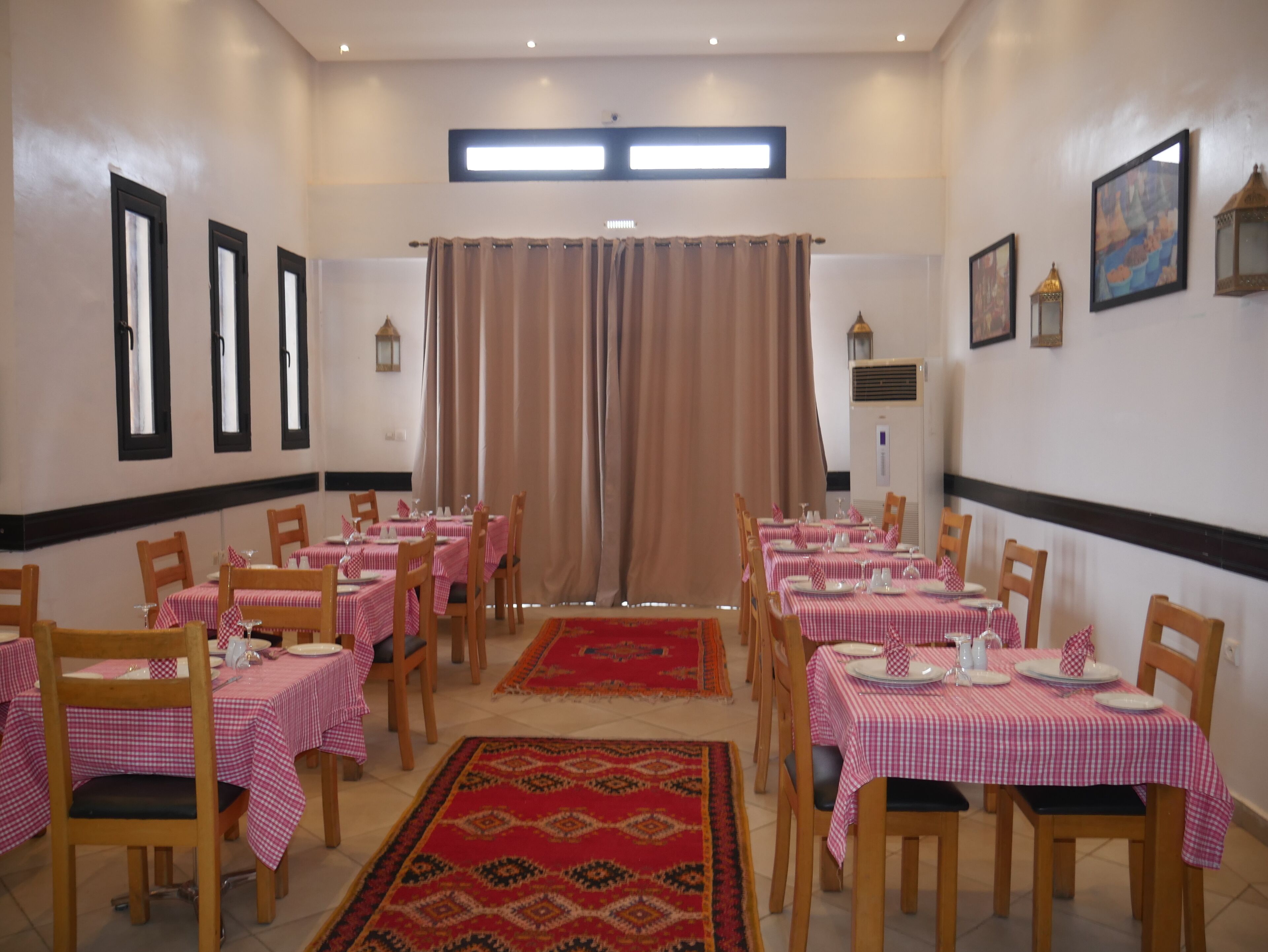 A dining area with tables set for four, each with a checkered tablecloth and wooden chairs.
