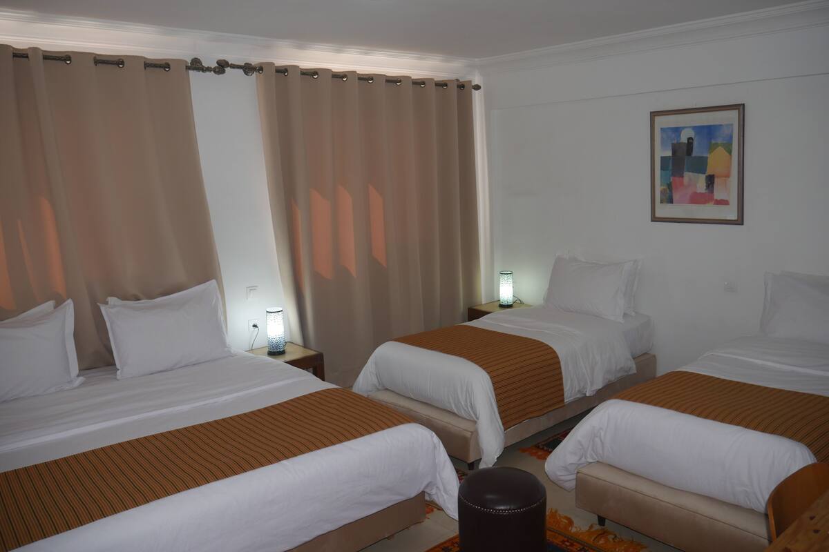 A hotel room with two beds, a nightstand with a lamp, a painting on the wall, and a window with curtains.