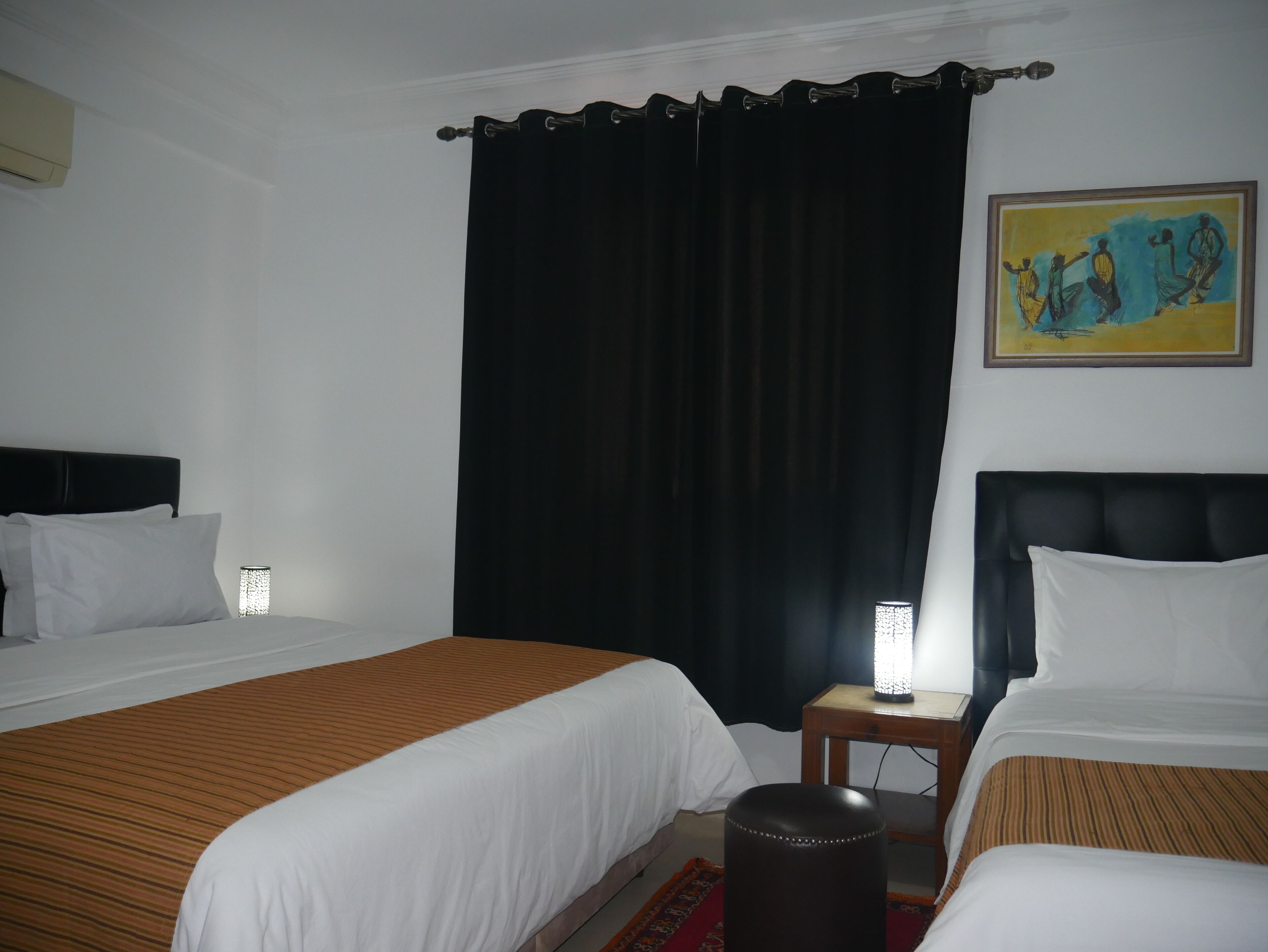 Habitación de hotel con dos camas, una mesita de noche con lámpara, un cuadro en la pared y una cortina negra.