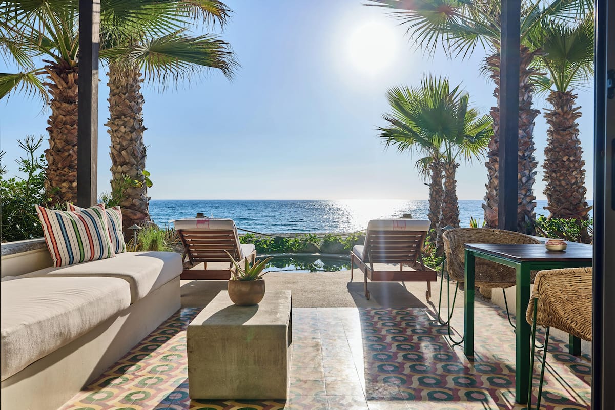 A sunlit outdoor seating area with a view of the sea, featuring a sofa, chairs, and a small table.