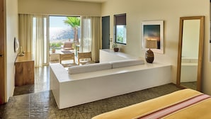 Una habitación de hotel moderna con una cama grande, un área de descanso con vista al océano y un balcón con mobiliario exterior.