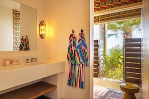 A bathroom with a white sink, two faucets, a mirror, and a towel rack with colorful towels. - Hotel San Cristobal (Todos Santos)