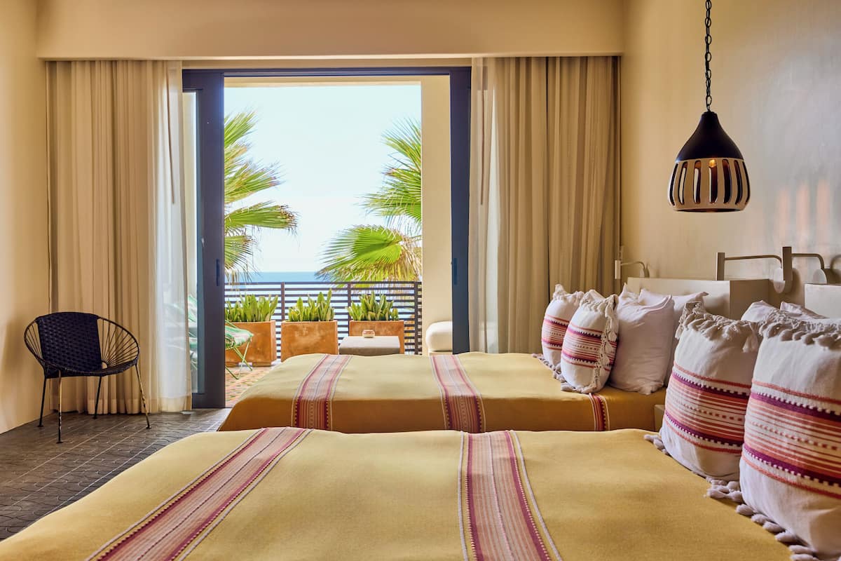 A hotel room with two beds, a view of the ocean, and a hanging light fixture.