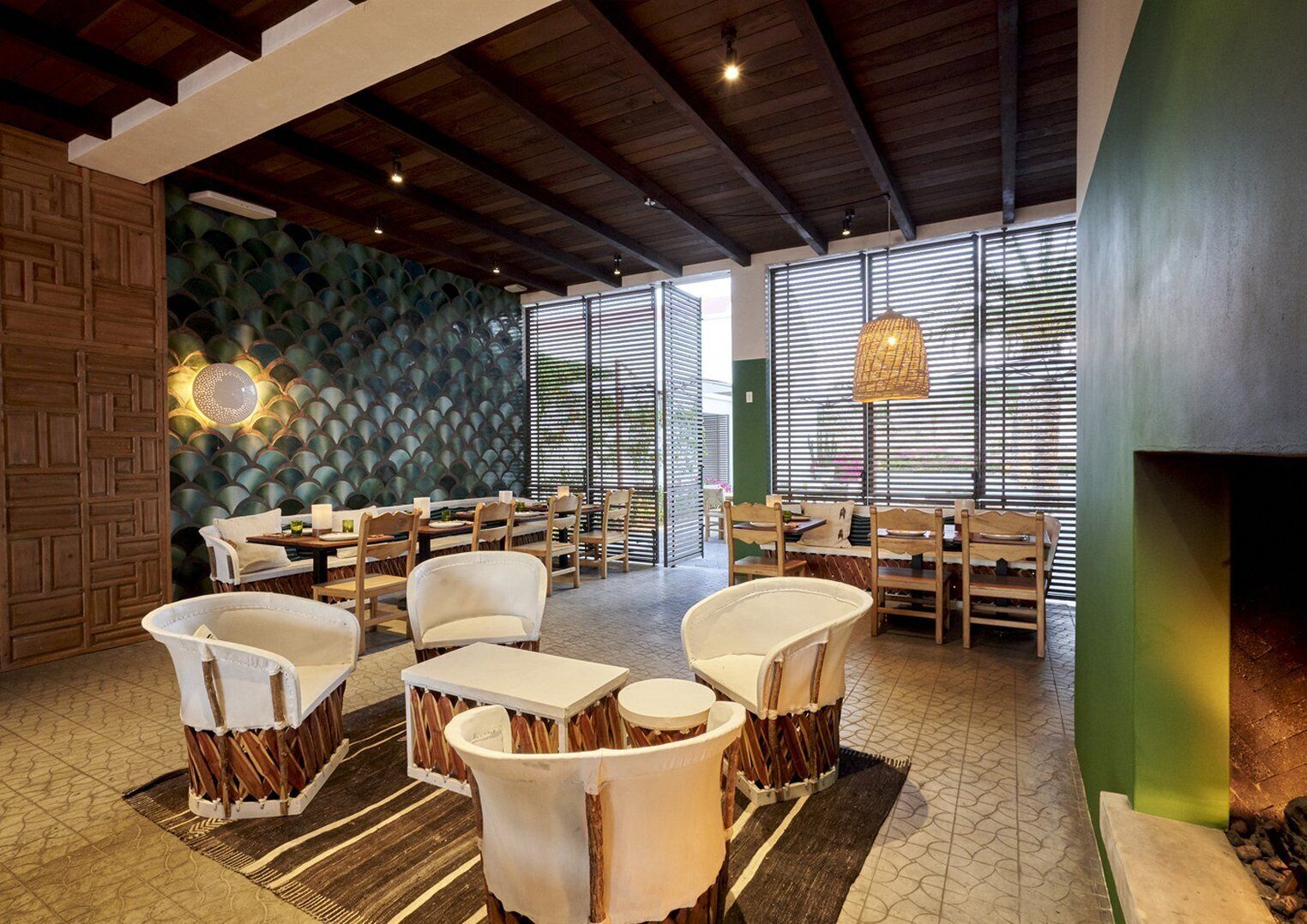 A spacious indoor area with multiple dining tables and chairs, a decorative wall with a geometric pattern, and a hanging light fixture.