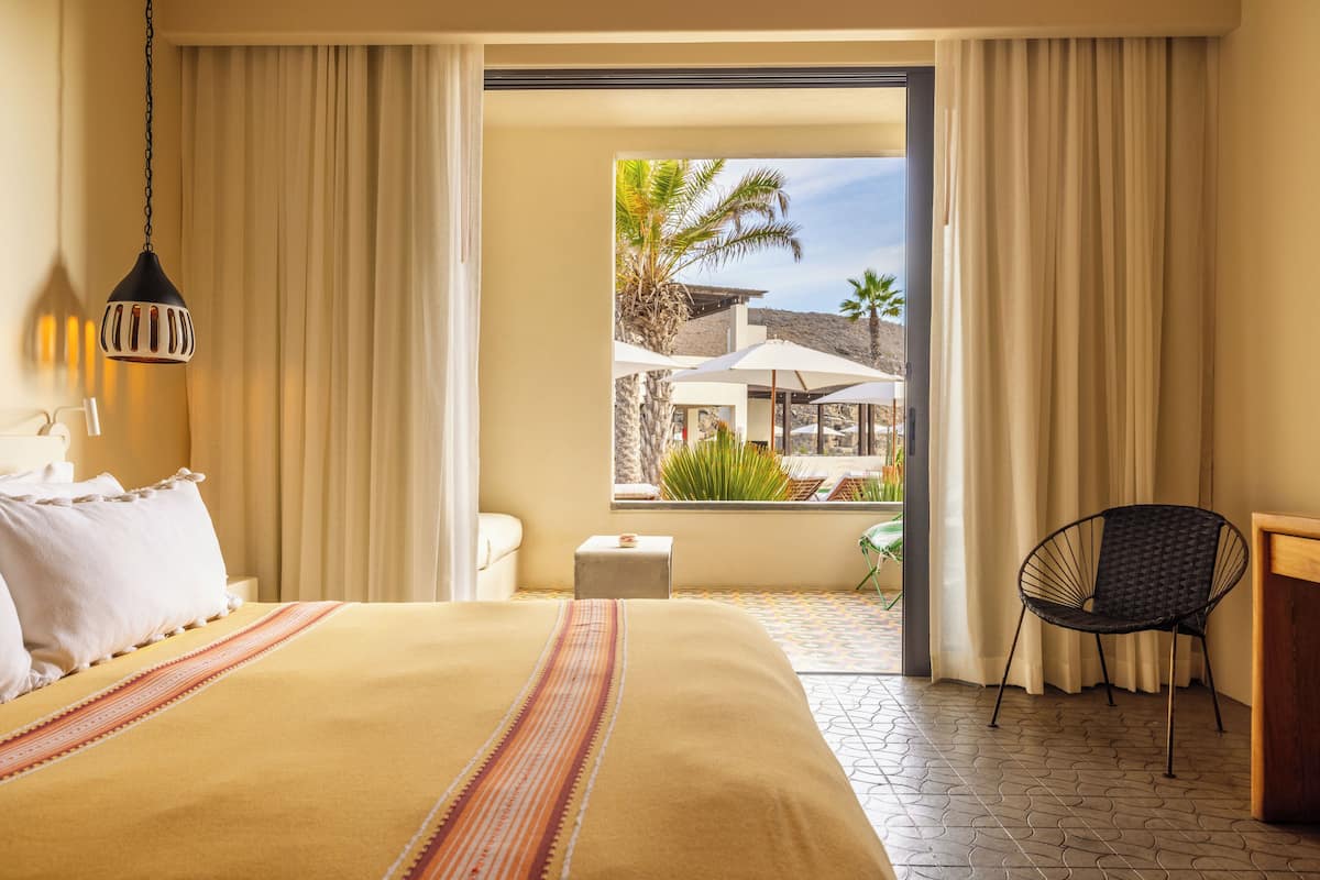 A hotel room with a bed, a chair, a desk, and a view of the outdoor area.