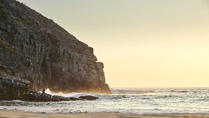 Paisaje costero con un acantilado rocoso y olas rompiendo en la orilla.