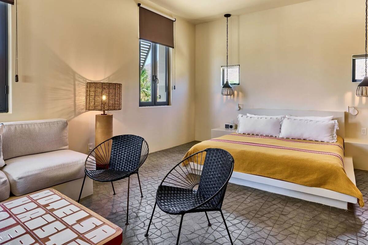 A bedroom with a bed, two chairs, a sofa, a lamp, and a small table.