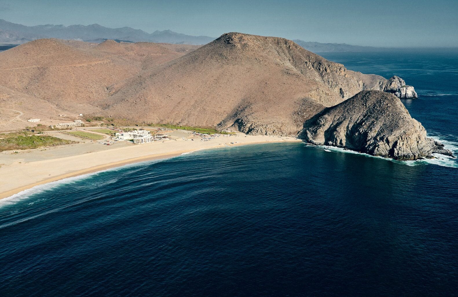 A coastal landscape with a sandy beach, a rocky outcrop, and a mountain in the background.