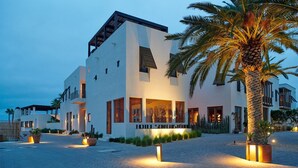 Un hotel moderno con fachada blanca, ventanas amplias y una palmera en primer plano.