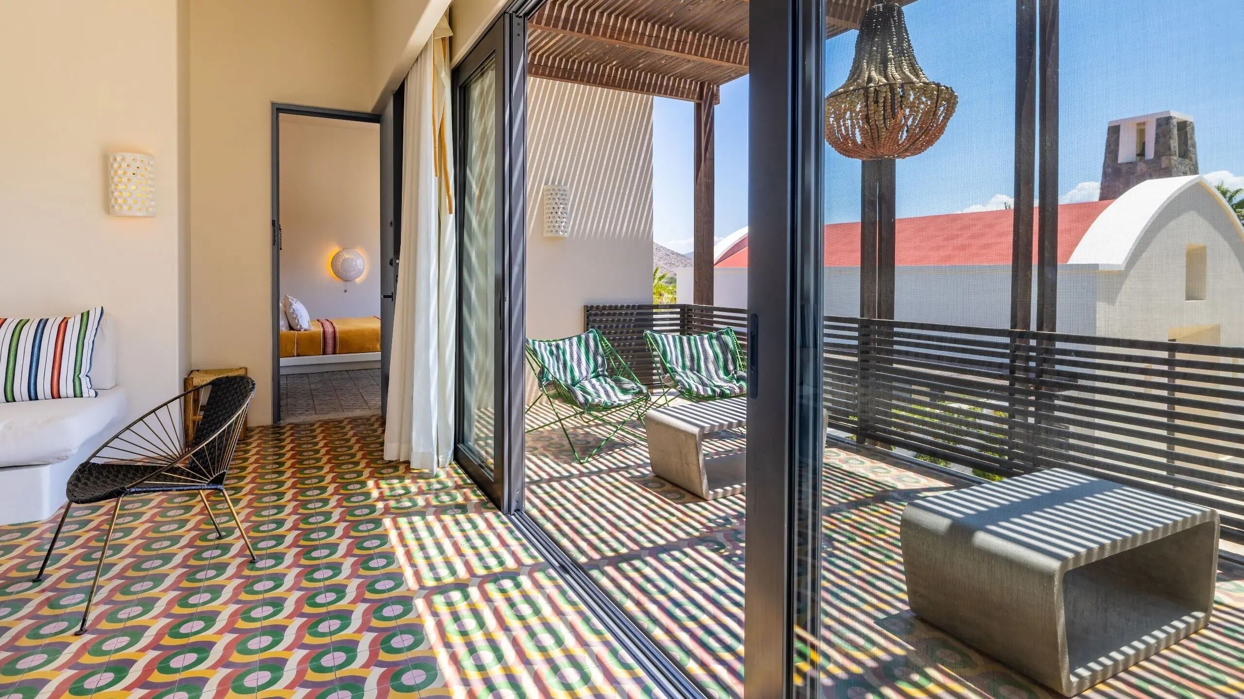 Uma varanda com piso estampado, um sofá, duas cadeiras e um lustre.