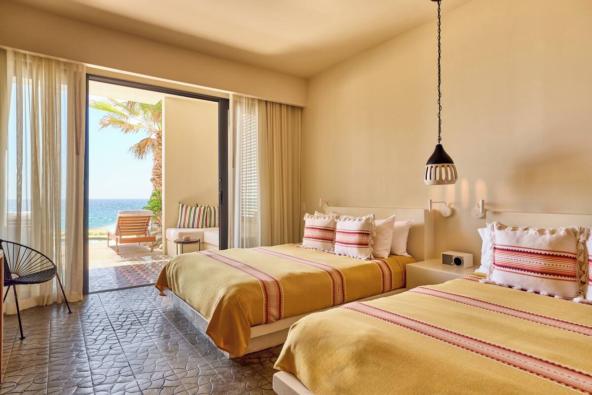 A hotel room with two beds, a view of the ocean, a chair, and a small table.