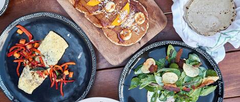 Une table en bois sur laquelle on trouve différents plats, notamment des crêpes, une salade et une assiette avec un morceau de poisson.