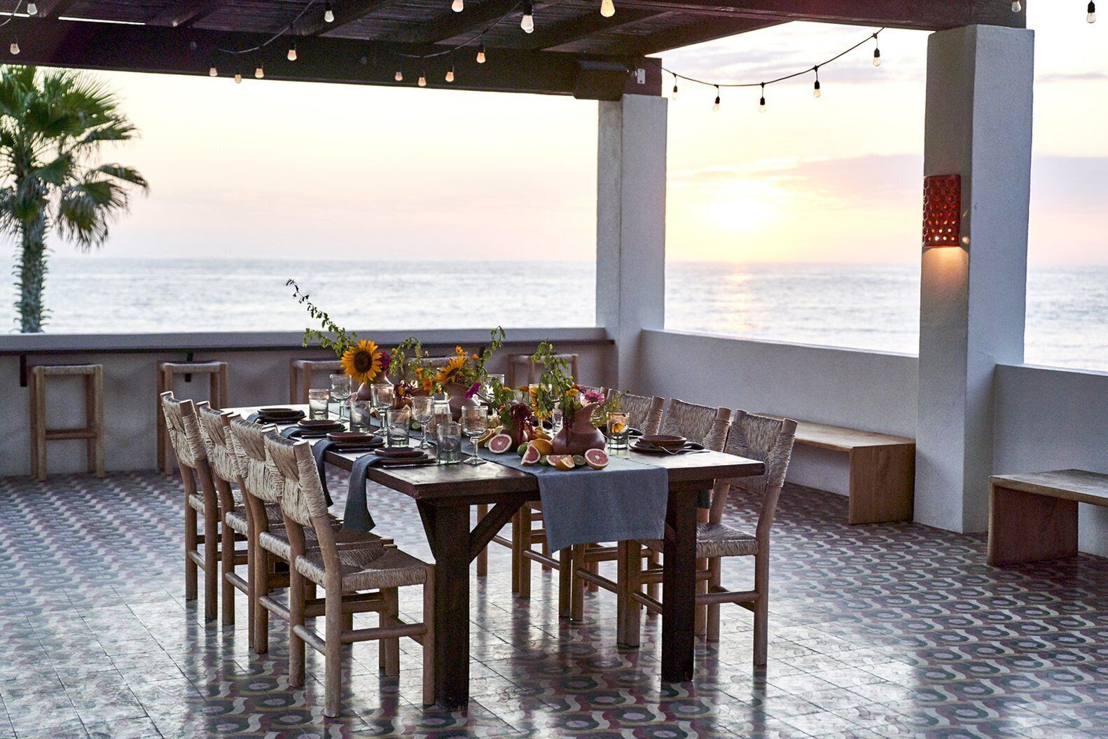 Un comedor con vistas al océano, con una mesa dispuesta con platos, vasos y un jarrón de flores.