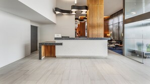 Una moderna zona de recepción con mostrador de mármol, detalles de madera y un separador de vidrio.
