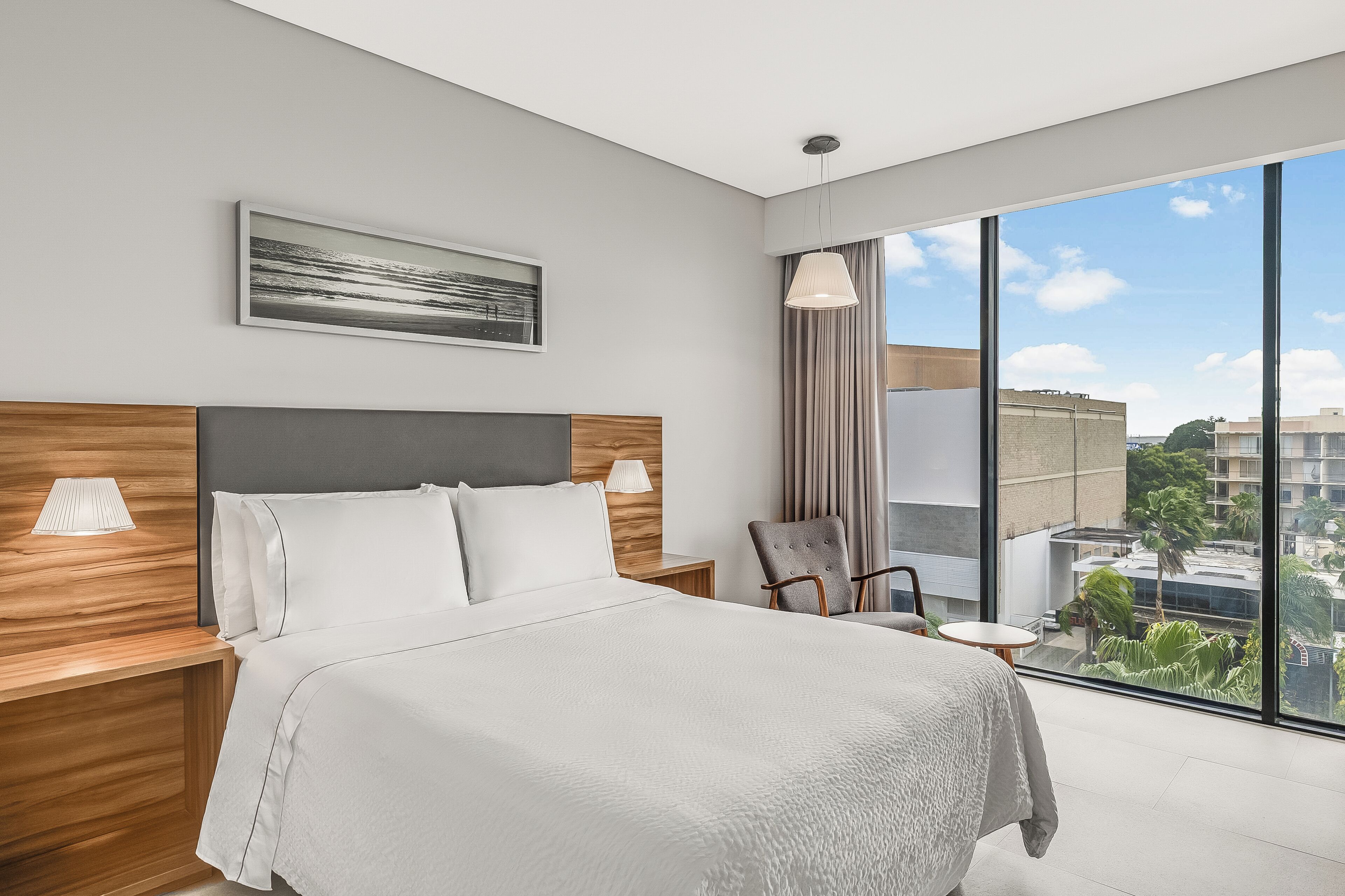 Una camera d'albergo moderna con un letto grande, un tavolino, una sedia, una lampada e una grande finestra con vista sulla città.