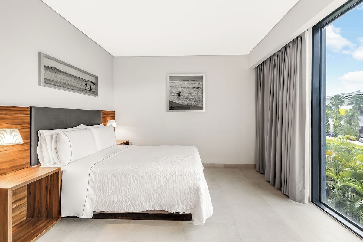 Un dormitorio moderno con una cama grande, una mesita de noche de madera, una lámpara de noche y dos cuadros en la pared.