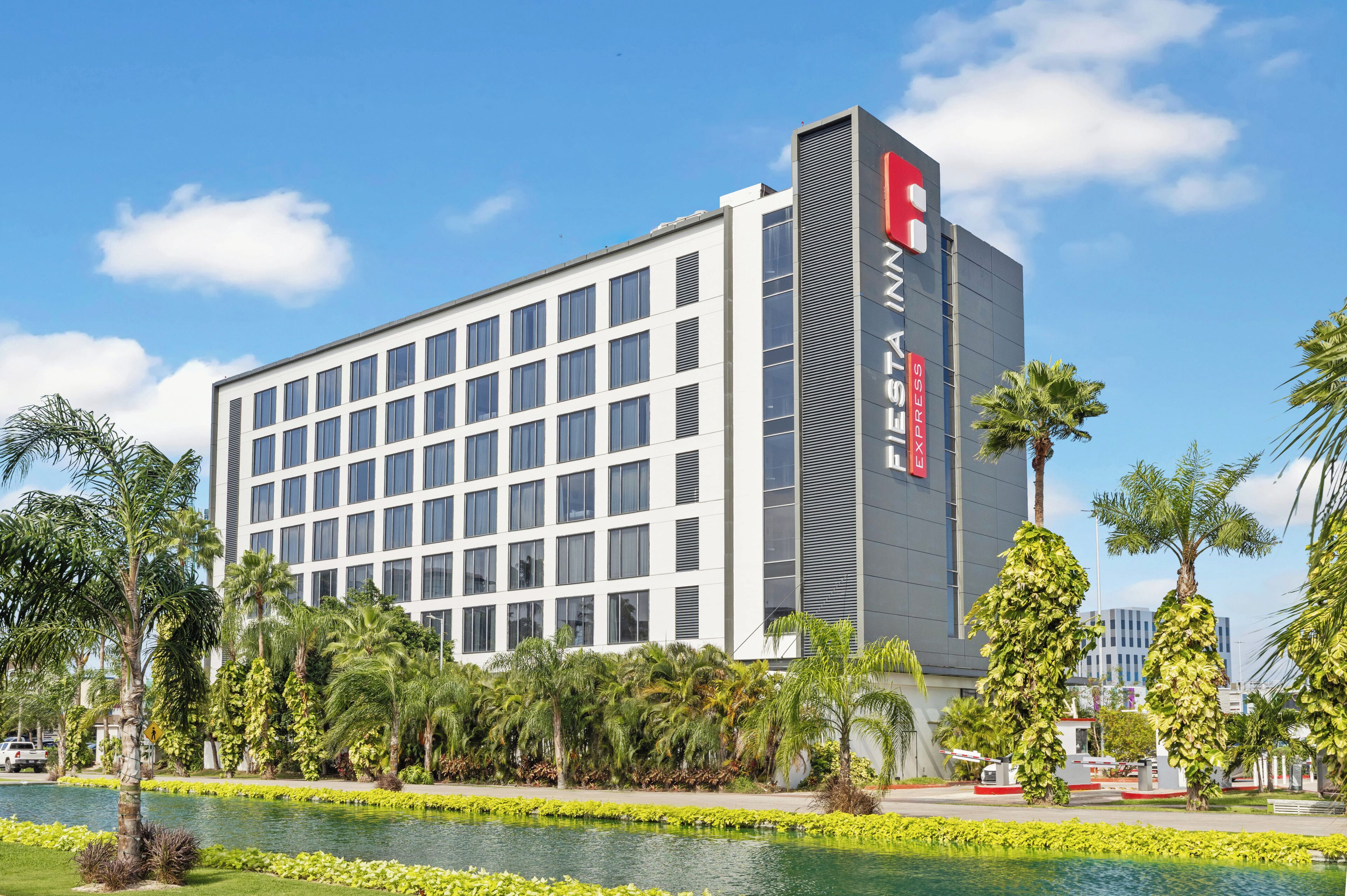 Um hotel moderno com um logotipo vermelho marcante, rodeado por palmeiras e uma fonte ornamental.