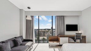 Una habitación de hotel moderna con un ventanal grande, una cama, un sofá, un escritorio y una silla.