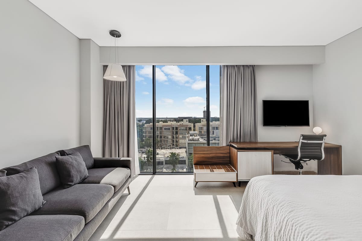 Una habitación de hotel moderna con un ventanal grande, una cama, un sofá, un escritorio y una silla.