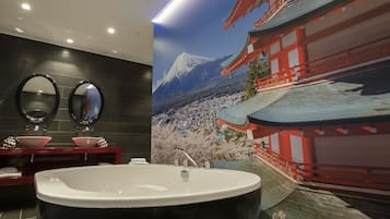 A modern bathroom with a large bathtub, two round mirrors, and a red sink.