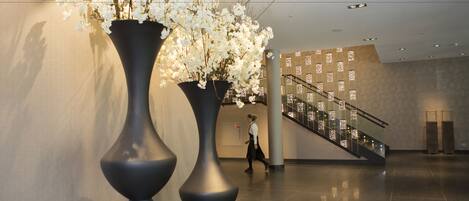 A spacious lobby with a large vase of white flowers, a staircase, and a modern design.