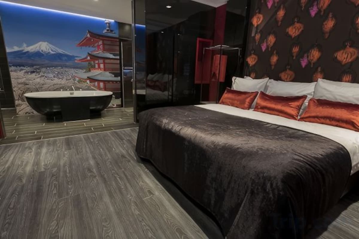 A modern bedroom with a large bed, a bathtub, and a wall mural of a mountain and pagoda.
