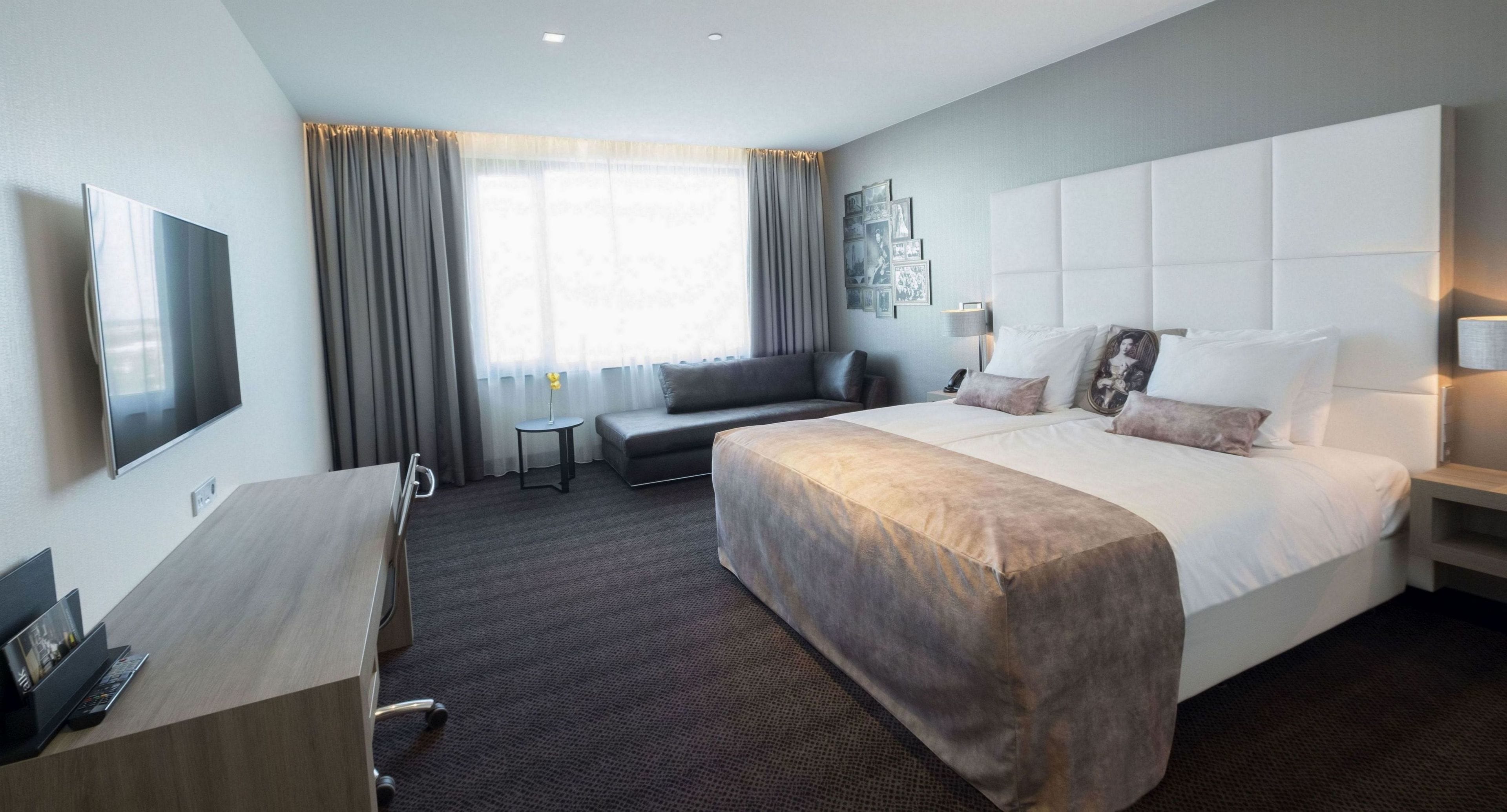 A hotel room with a large bed, a desk, a TV, and a sofa.