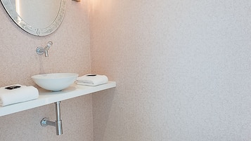 Un baño con un lavabo blanco, un espejo grande, una lámpara empotrada en la pared y un inodoro.