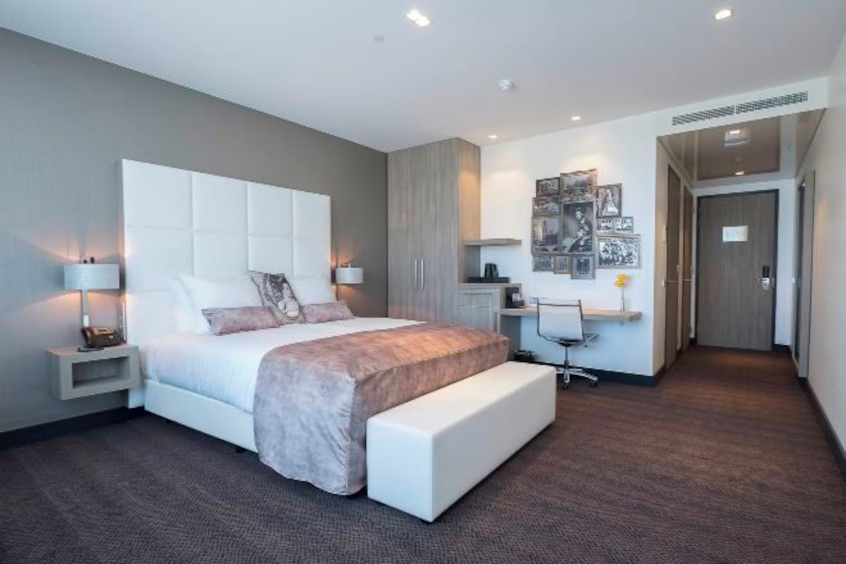 A modern hotel room with a large bed, bedside tables, a desk, and a bench.