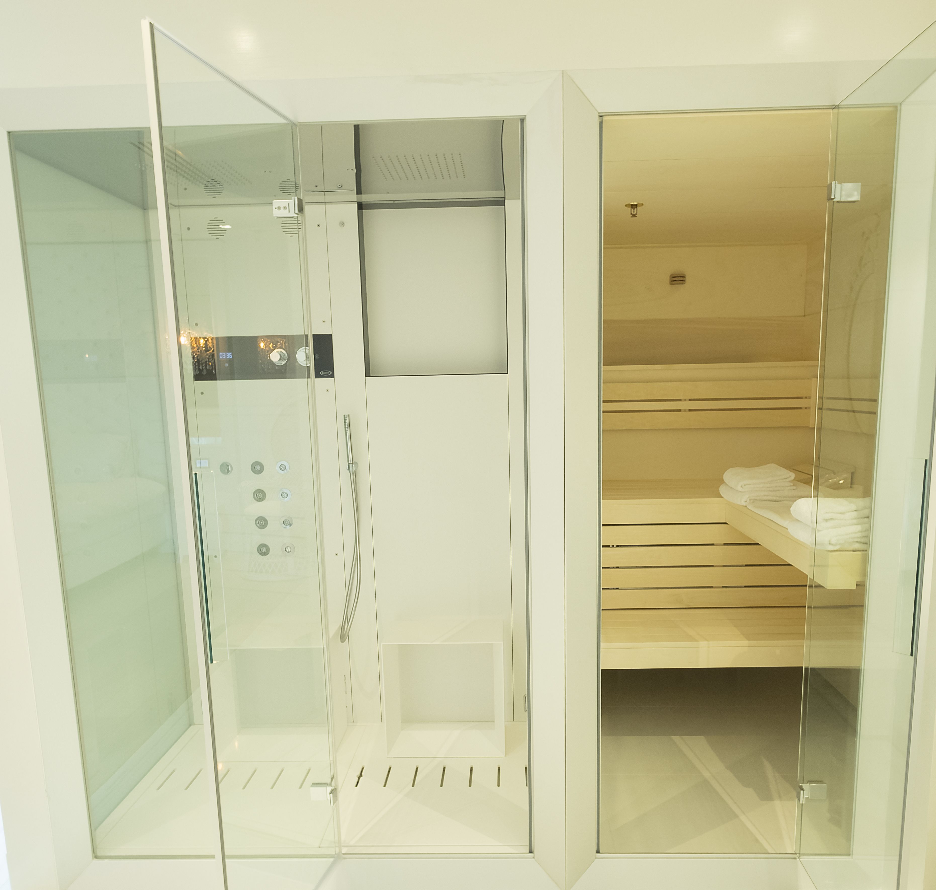 Un baño moderno con cabina de ducha de vidrio, toallero empotrado y panel de control a la vista.
