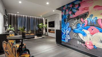 A modern living room with a fireplace, a dining area with graffiti-covered chairs, and a colorful mural on the wall.