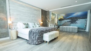 Un dormitorio moderno con una cama grande, un rincón de descanso y un mural de paisaje costero.