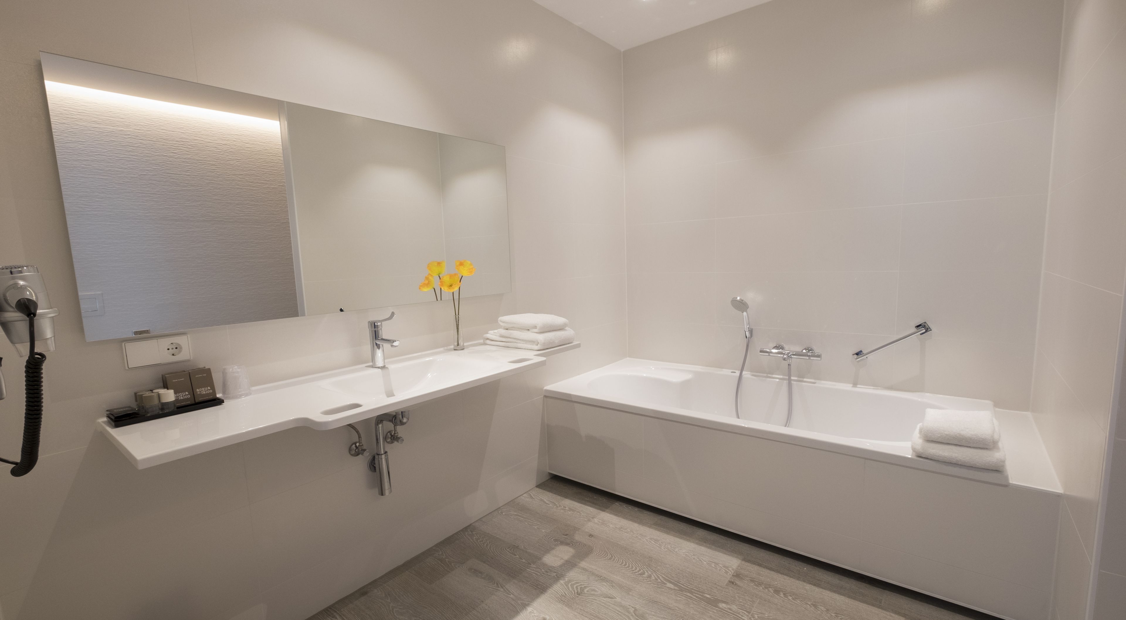 Un baño moderno con un espejo grande, dos lavamanos, una bañera y un secador de pelo en la pared.