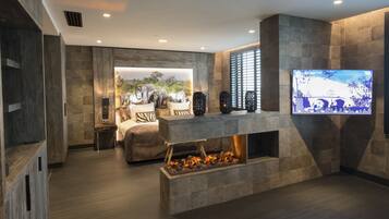 A modern living room with a fireplace, a television mounted on the wall, and a large window with blinds.