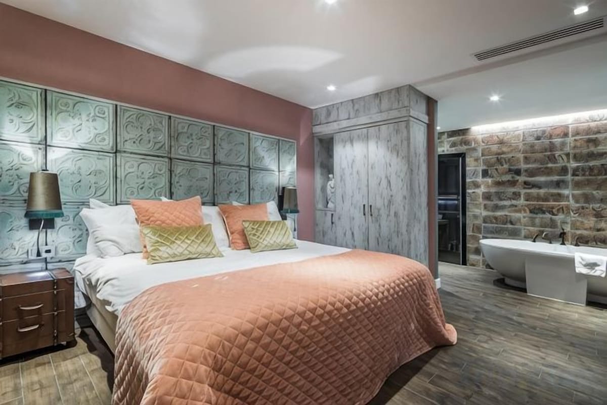 A modern bedroom with a large bed, a built-in wardrobe, and a bathroom with a bathtub.