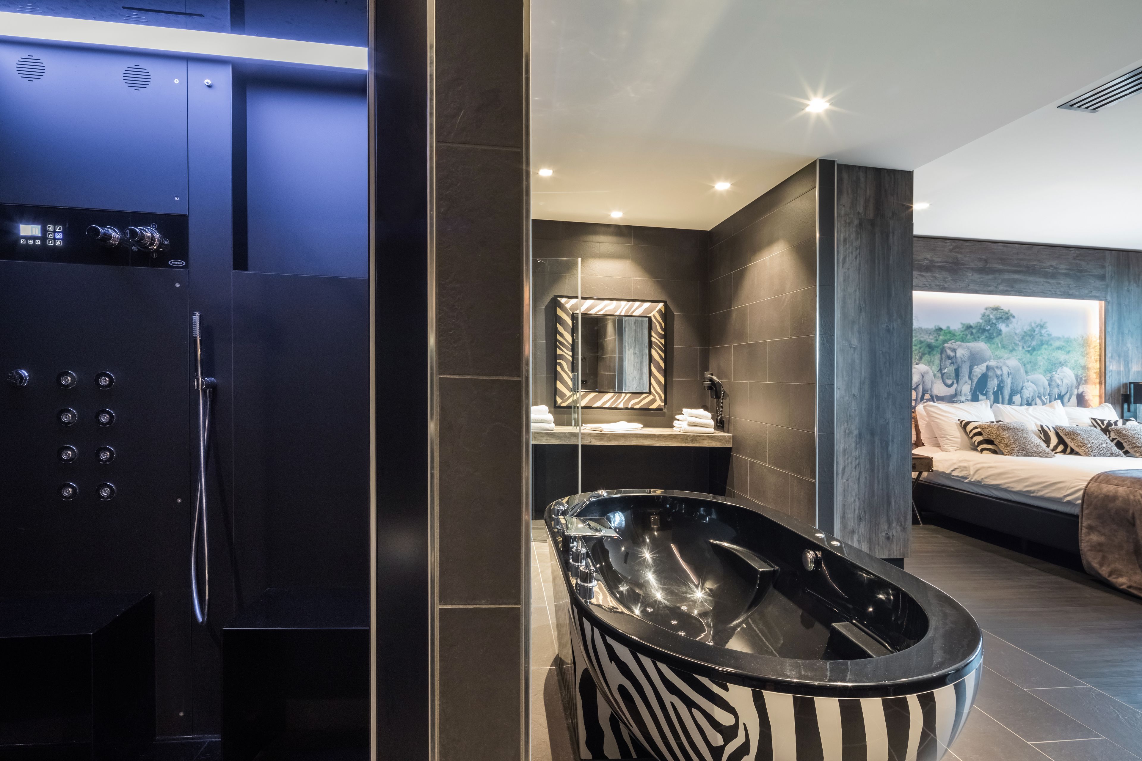 Un baño moderno con una bañera negra grande, zona de ducha y tocador con espejo.