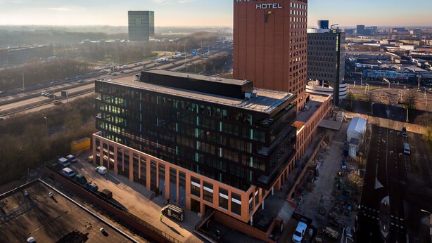 Un hotel moderno con un llamativo letrero que dice 'HOTEL', rodeado de otros edificios y una autopista.