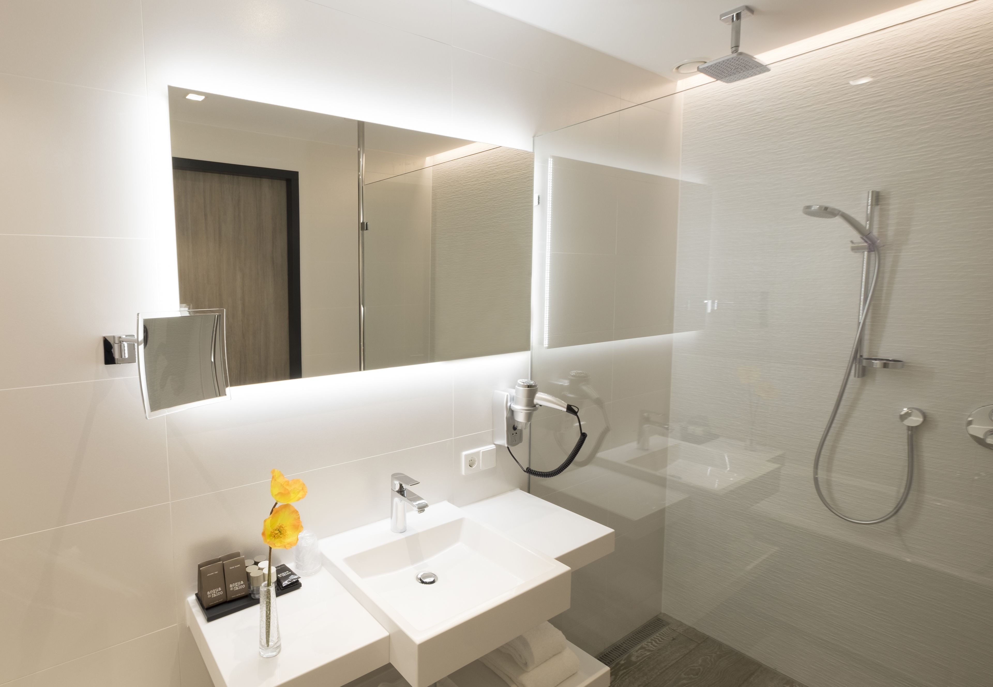 Ein modernes Badezimmer mit Waschbecken, Spiegel und Dusche in Weiß.