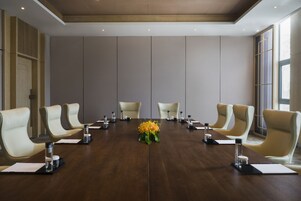 Un salón de conferencias con una larga mesa, seis sillas y un jarrón de flores.