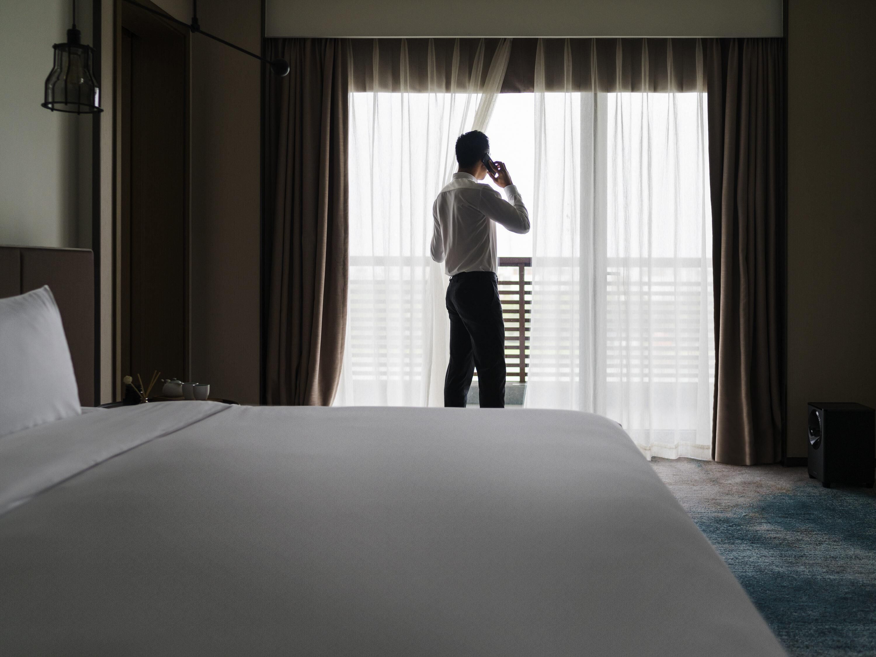 A hotel room with a large bed, a window with curtains, a bedside lamp, and a small table with a candle.