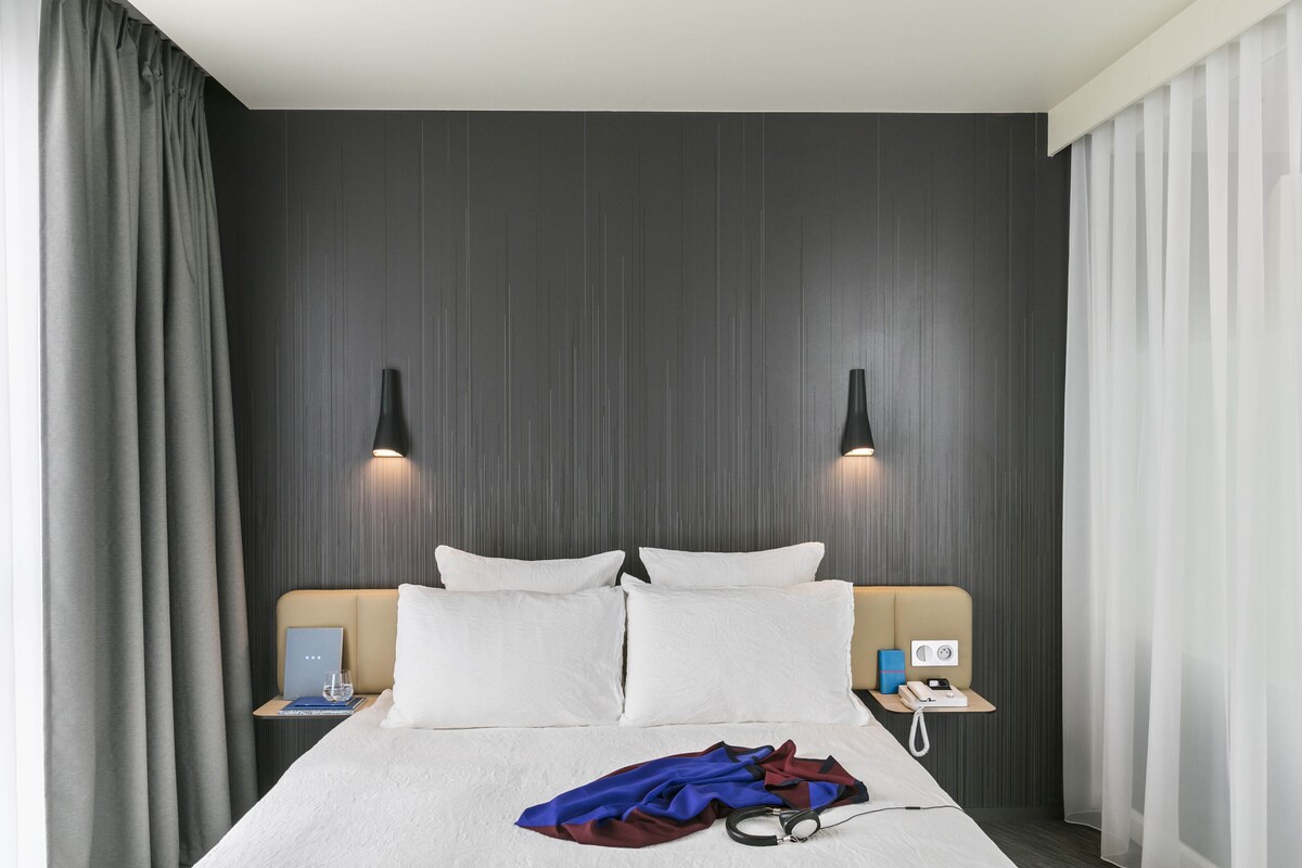 A hotel room with a bed, two bedside tables, a lamp, and a curtain.