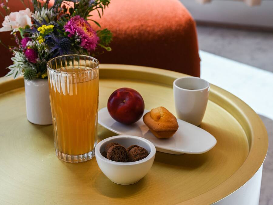 A tray with a glass of orange juice, a plum, a muffin, and a bowl of cookies on a round table.