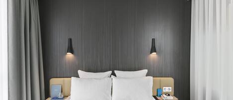 A hotel room with a bed, two bedside tables, a lamp, and a curtain.
