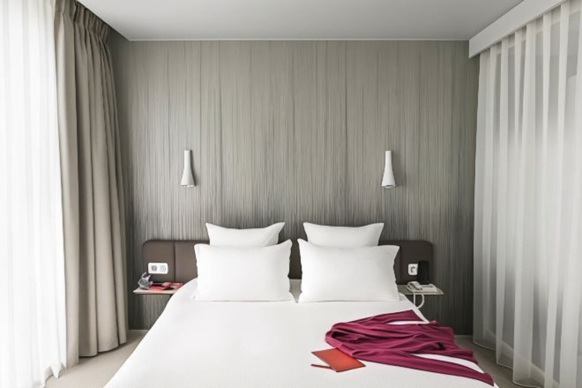 Una habitación de hotel con una cama grande, dos mesitas de noche y un cabecero con iluminación integrada.
