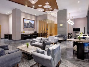 A modern hotel lobby with grey sofas, a marble coffee table, a TV, and a large painting on the wall.