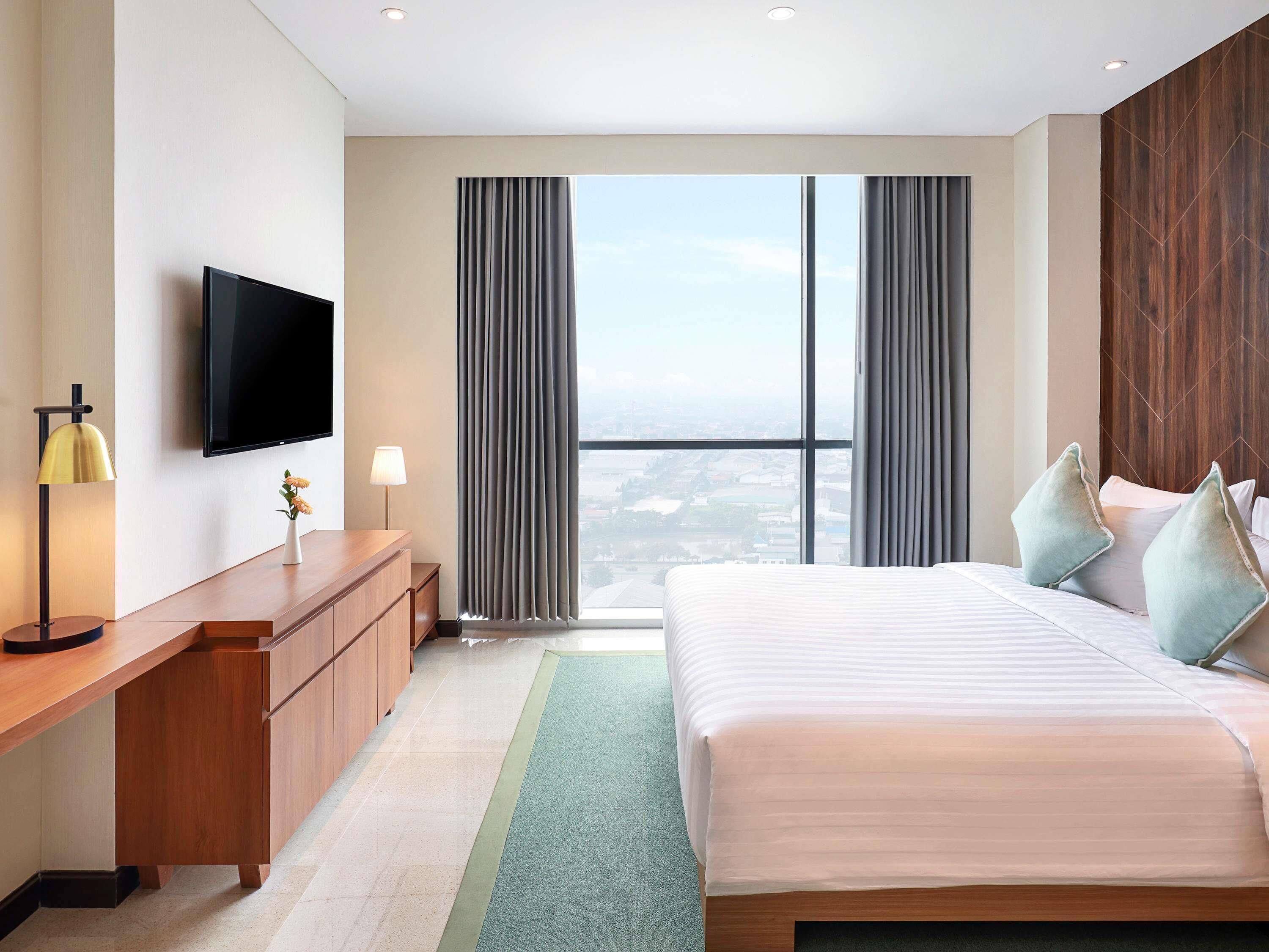 Ein Hotelzimmer mit Bett, Schreibtisch, Fernseher und Blick auf die Stadt.